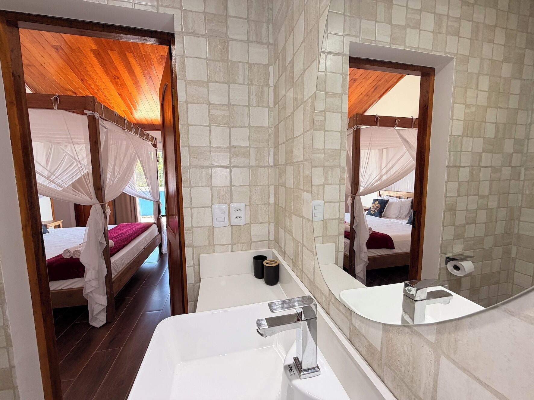 A bedroom with a canopy bed, a bathroom with a sink and mirror, and a stone-tiled wall.