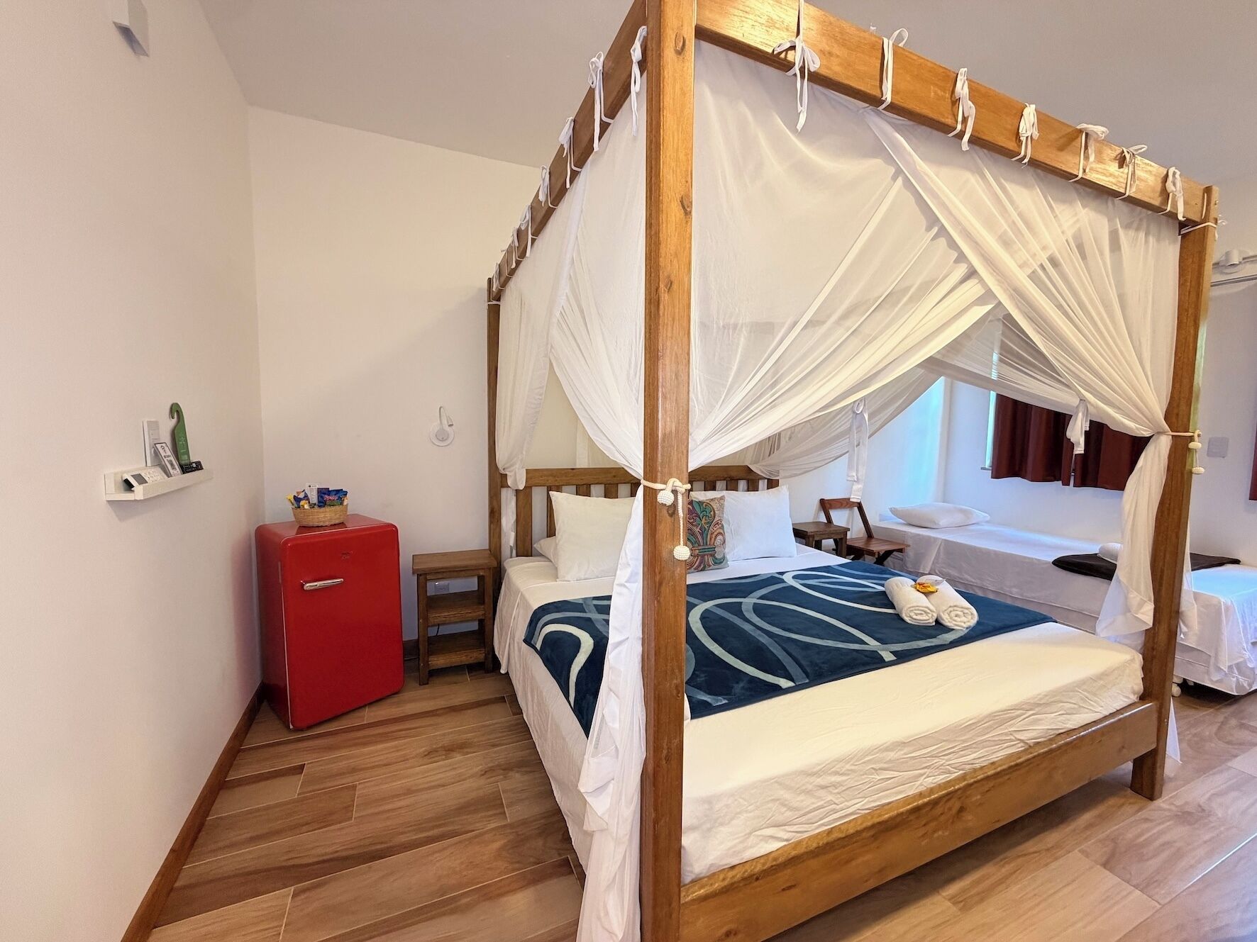 Un lit à baldaquin, une commode rouge, une petite table en bois et une table de chevet avec une lampe.