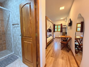 Una habitación con puerta de madera, ducha, cama con dosel, mesa y un banco.
