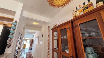 A hallway with a wooden cabinet containing glassware, a woven light fixture, and a row of blue mugs on the wall.