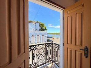 Un balcón con barandilla de hierro forjado y vista a un edificio con ventanas arqueadas y tejado de tejas.