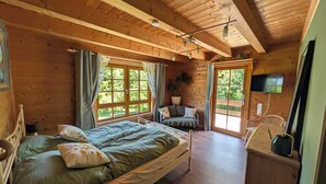 A wooden cabin bedroom with a bed, a sofa, a TV, and a window with curtains.