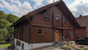 A two-story wooden house with a sloped roof, a front door, and a small porch area.