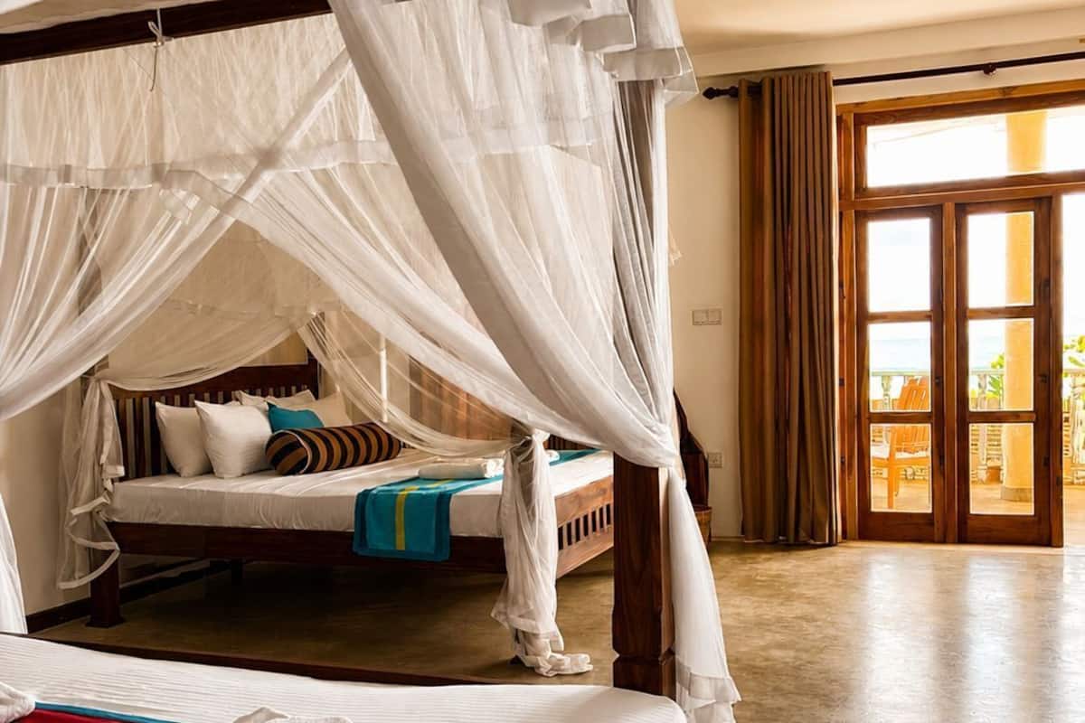 A room with a four-poster bed, a smaller bed, and a large sliding glass door leading to an outdoor area.
