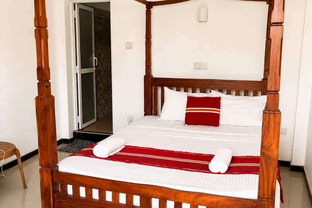 A four-poster bed with a wooden frame, white bedding, and red accents.