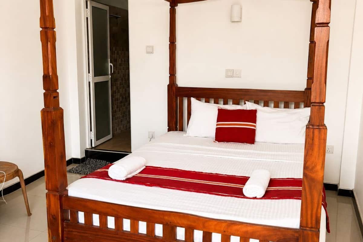 A four-poster bed with a wooden frame, white bedding, and red accents.