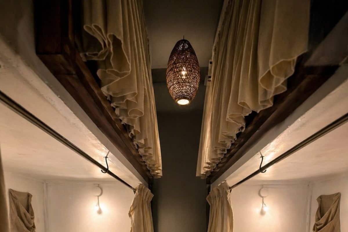 A narrow corridor with bunk beds, each with a hanging light fixture and curtains.
