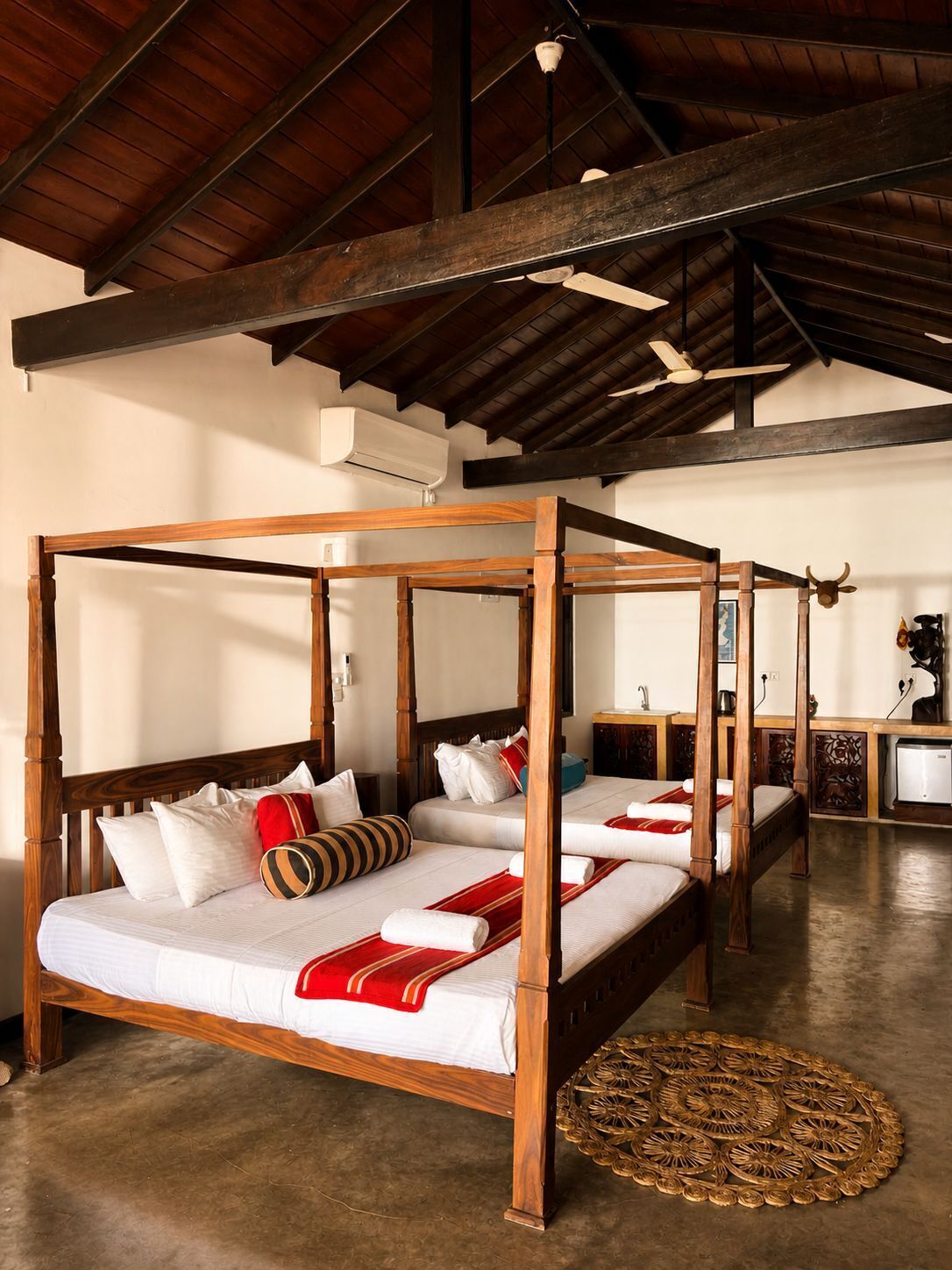 A room with four wooden four-poster beds, a woven floor mat, and a ceiling fan.