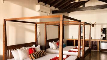 A room with four wooden four-poster beds, a woven floor mat, and a ceiling fan.