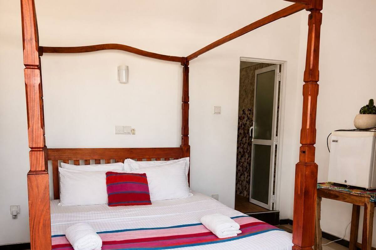 A four-poster bed with a checkered bedspread, white pillows, and a red and blue striped pillow.