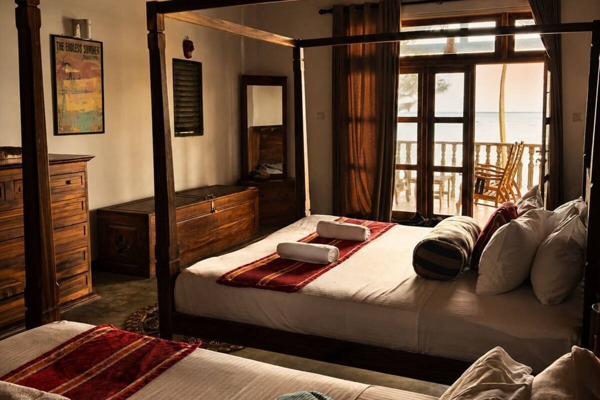A four-poster bed with a view of the beach, wooden furniture, and a ceiling fan.