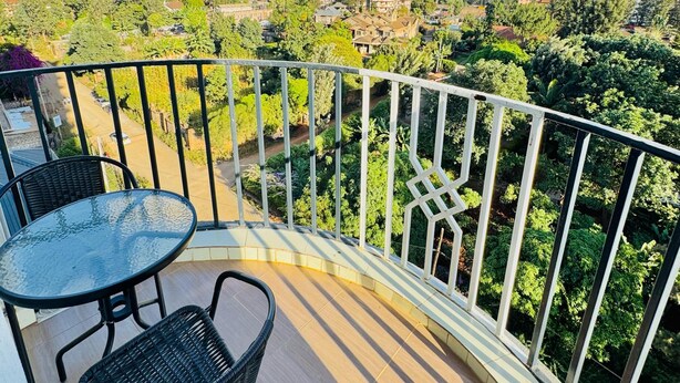 A balcony with a table and chairs, a railing, and a view of a cityscape with buildings and trees. - Peaceful 1-bedroom corporate apartment in vibrant Nairobi (Nairobi)