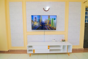 Ein an der Wand befestigter Fernseher, darunter eine weiße Unterhaltungseinrichtung und ein kleiner Tisch mit einer Vase.
