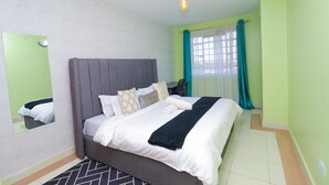 A neatly made bed with a grey headboard, a mirror on the wall, and a hanging light fixture. - Peaceful 1-bedroom corporate apartment in vibrant Nairobi (Nairobi)