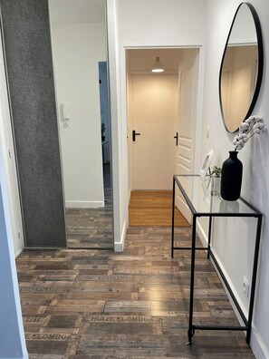 Ein Flur mit Holzboden, einem Glastisch mit einer Vase und einem Spiegel an der Wand.
