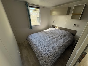 Une chambre à coucher avec un lit, une fenêtre avec des rideaux, une table de chevet et des placards intégrés.