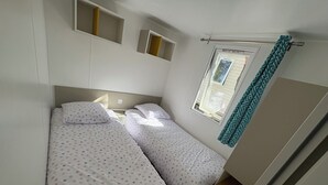 Een slaapkamer met twee bedden, een raam met gordijnen en inbouwplanken.