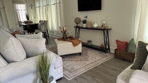 A living room with a sofa, ottoman, coffee table, and a TV mounted on the wall. - LSU BOUND! We are minutes from everything! (Baton Rouge)