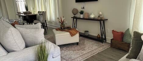 A living room with a sofa, ottoman, coffee table, and a TV mounted on the wall.