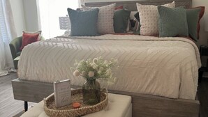A bedroom with a bed, pillows, a bedside table with a book and flowers, a chair, and a rug. - LSU BOUND! We are minutes from everything! (Baton Rouge)