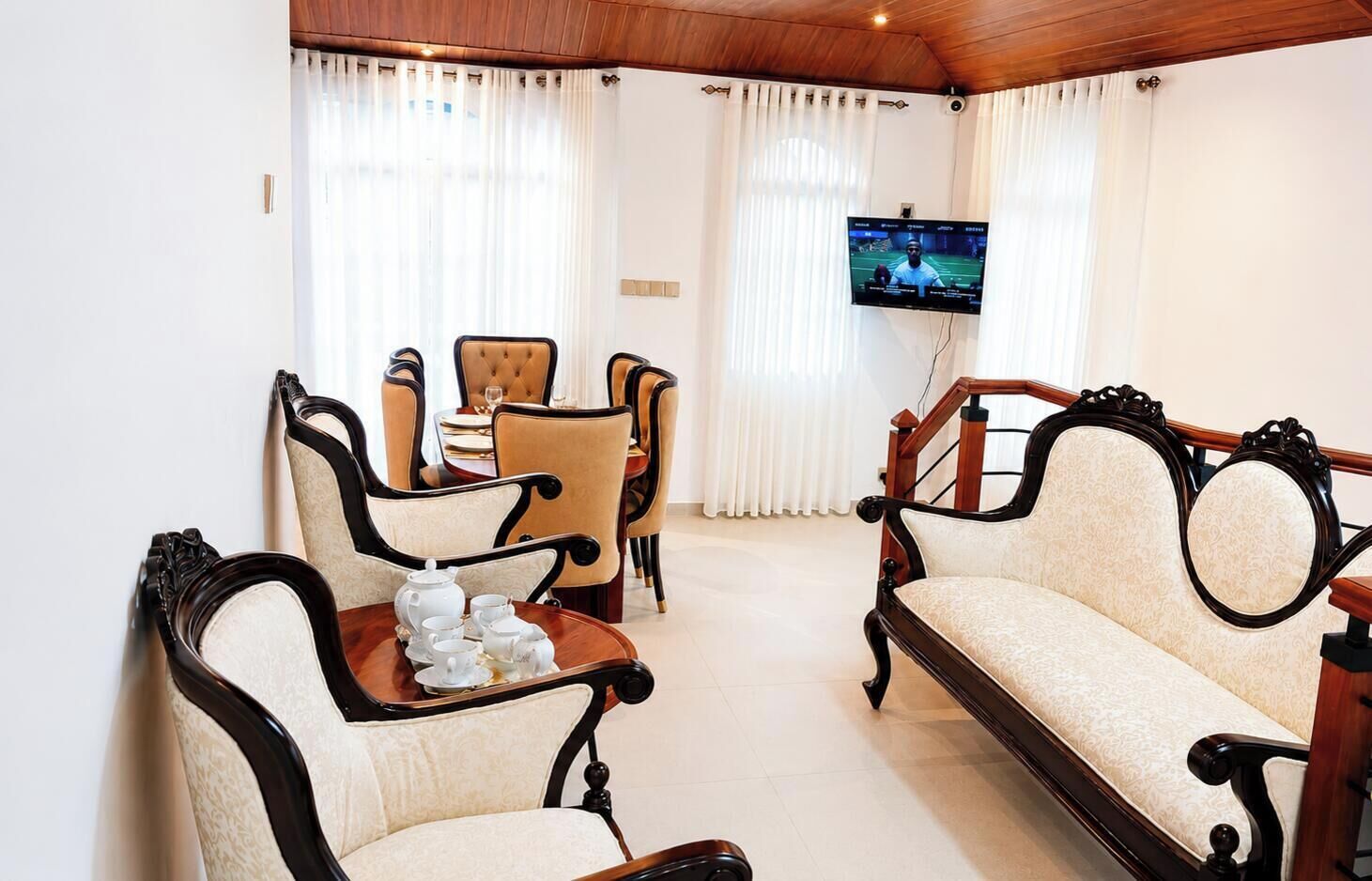 A living room with a sofa, chairs, a table with teapots, a television, and a dining area with a table and chairs.
