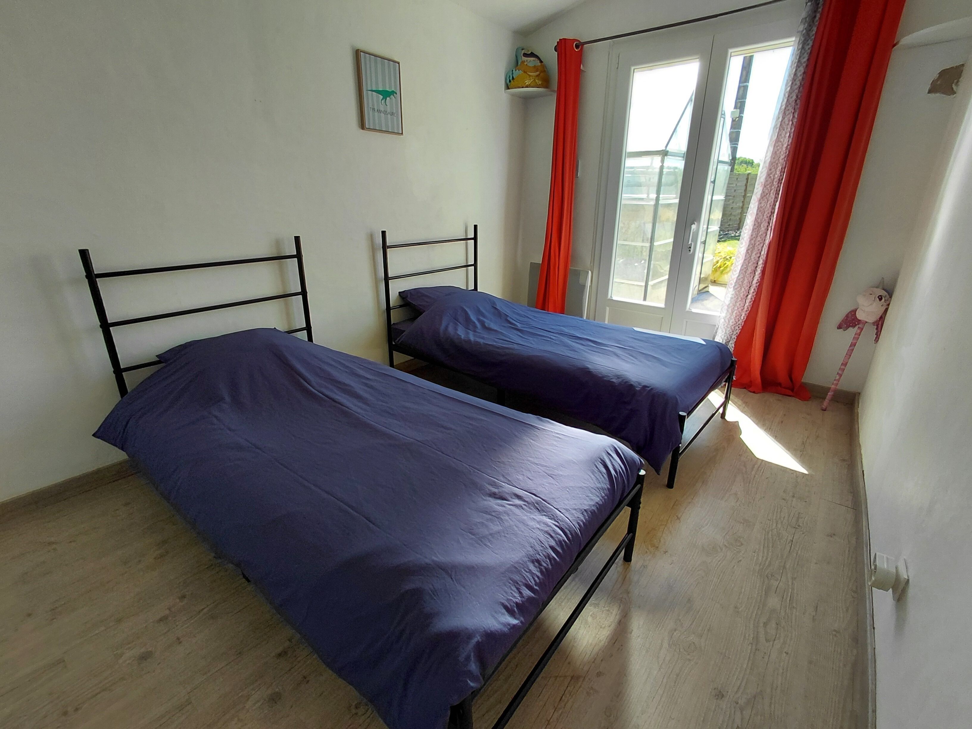 Une chambre avec deux lits, une fenêtre avec des rideaux, une porte et un petit élément de décoration murale.