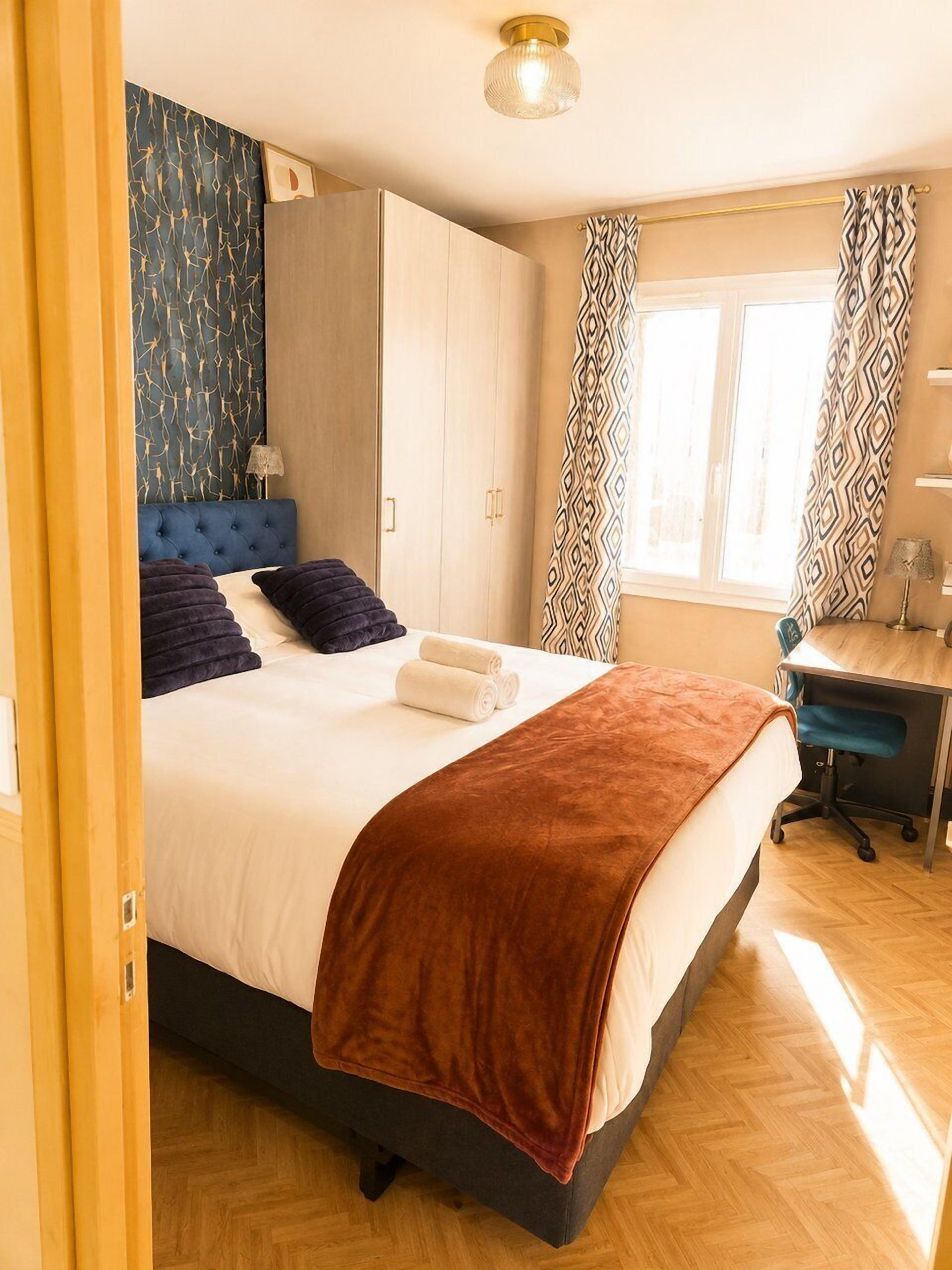 Une chambre à coucher avec un lit, un bureau, une armoire et une fenêtre avec des rideaux.