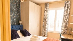 Une chambre à coucher avec un lit, un bureau, une armoire et une fenêtre avec des rideaux.