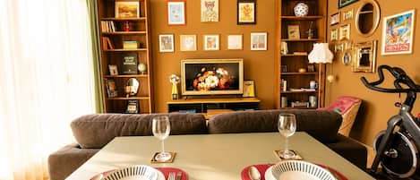 A dining area with a table set for two, a sofa, and a bookshelf with various items.