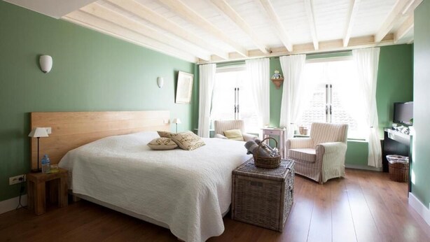 A bedroom with a large bed, a wooden ceiling, a small table, a chair, and a television. - The Abiente Rooms (Bruges)