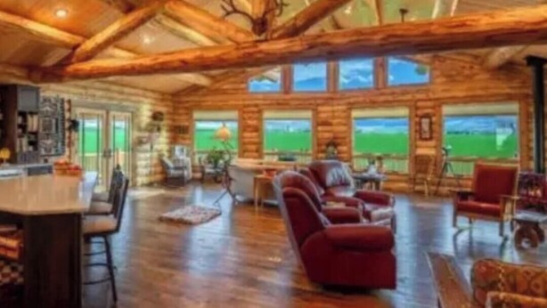 A log cabin interior with a bar area, seating, and large windows.