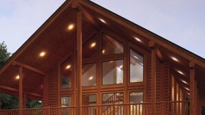A wooden cabin with a balcony, large windows, and a staircase.