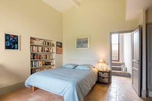 Ein Schlafzimmer mit Bett, Bücherregal, Nachttisch, Lampe und einer Treppe, die in einen Außenbereich führt.