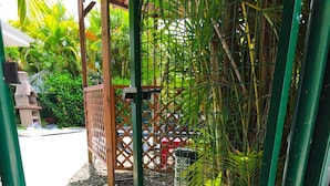 A gated outdoor area with a concrete path, a wooden structure, and dense foliage.