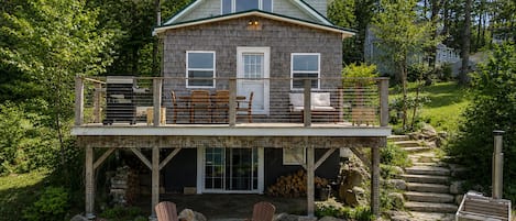 Uma casa de dois andares com varanda, deck de madeira e área de estar externa.