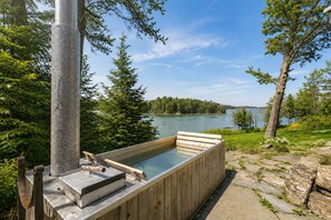 Ein Whirlpool mit Holzterrasse, umgeben von Bäumen und Blick auf einen See.