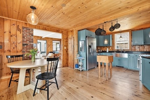 Ein Holzinterieur mit einem Esstisch, Stühlen, einer Küche mit blauen Schränken und einer hängenden Küchenutensilienstange.