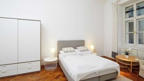 Een slaapkamer met een bed, nachtkastjes, een garderobe, een raam en een klein rond tafeltje met een stoel.