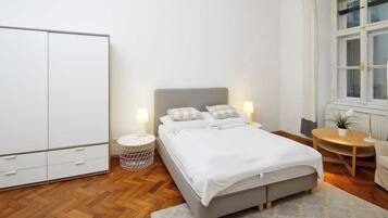 Une chambre à coucher comprenant un lit, des tables de chevet, une armoire, une fenêtre et une petite table ronde avec une chaise.