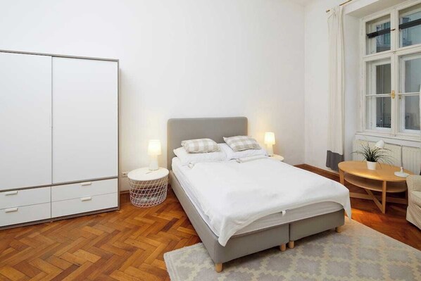 A bedroom with a bed, bedside tables, a wardrobe, a window, and a small round table with a chair.