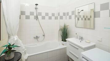 Une salle de bain avec une baignoire, une douche, un lavabo, un miroir et une plante en pot.