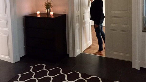 Een kamer met een donker houten dressoir, een zwarte hanglamp, een patroonrijk vloerkleed en een ingelijste foto aan de muur.