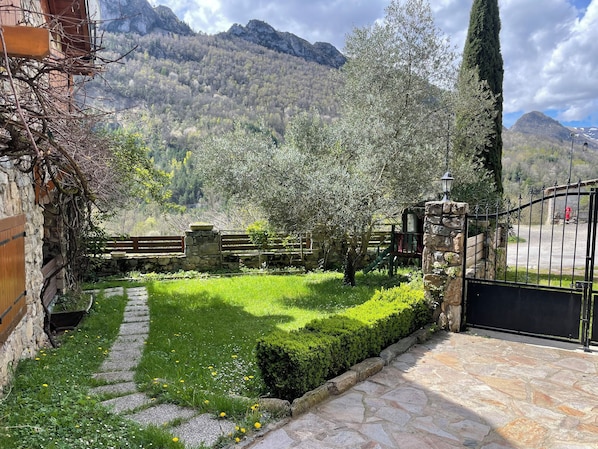 A stone pathway leading to a gate, a stone wall, and a wooden fence with a playground in a mountainous area. - Quiet mountain house (ARIGNAC)