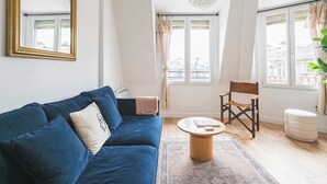 A living room with a blue sofa, a round wooden coffee table, a chair, and a large mirror.