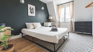 A modern bedroom with a bed, bedside table, lamp, dresser, and a large window with curtains.