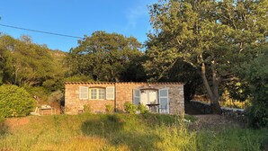 A stone cottage with a tiled roof, a small table, and a chair outside. - Charming house in a magnificent park facing the sea and its sunset (Pigna)