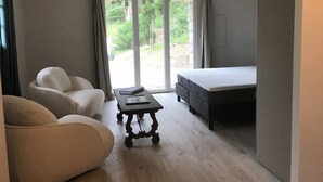 A bedroom with a bed, a chair, a table, and a view of the outdoors through a sliding door. - Charming house in a magnificent park facing the sea and its sunset (Pigna)