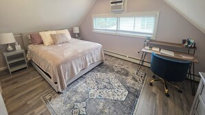 Ein Schlafzimmer mit einem Bett, Nachttischen, einem Schreibtisch, einem Stuhl, einem Deckenventilator, einer Klimaanlage und einem Fenster mit Jalousien.