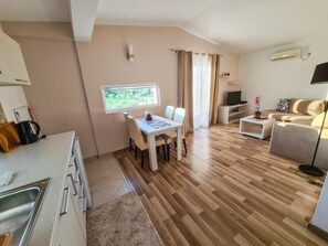 A modern living room with a dining table, sofa, TV, and a kitchen area with a sink and cabinets. - La Hacienda (Ulcinj)