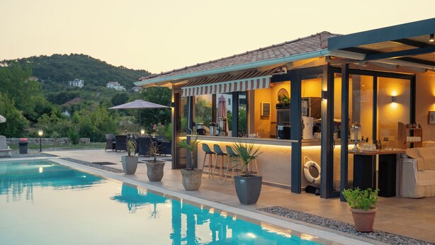 Zona de bar a la piscina amb seients exteriors, una piscina i una vista d'un turó.